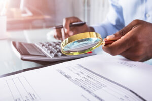 A private investigator with a calculator and a magnifying glass search for fraud that was committed.