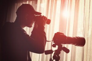 A person with a long lens camera peaking out a window to conduct surveillance.